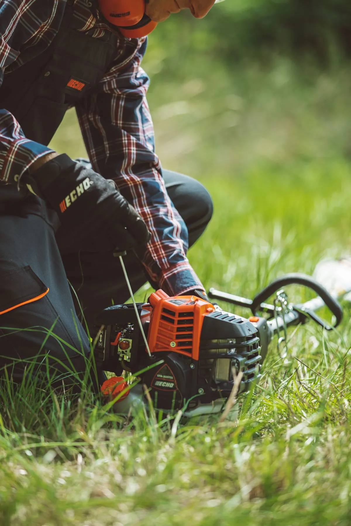 ECHO operator kneeling in grass next to a brushcutter