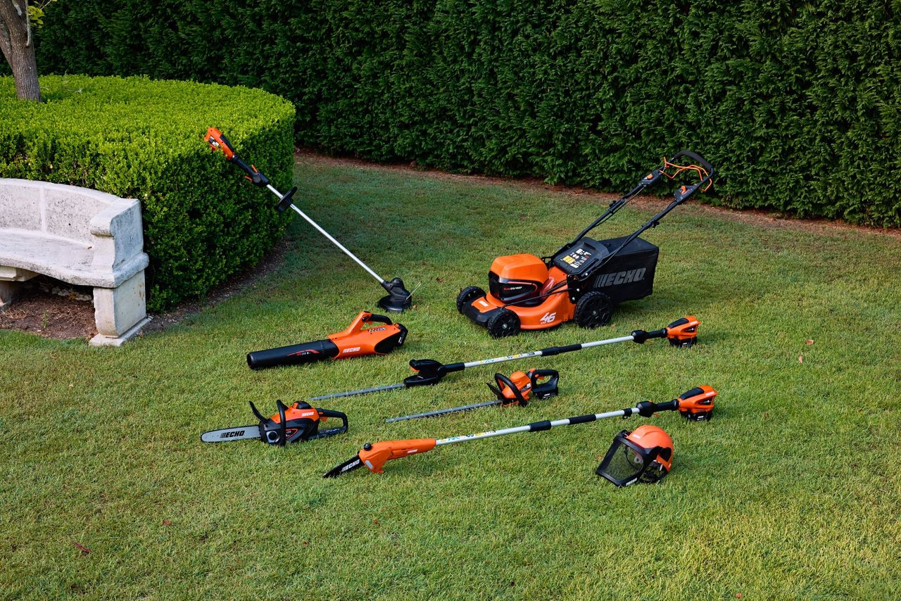 ECHO cordless garden tools laid out on a lawn next to a trimmed hedge